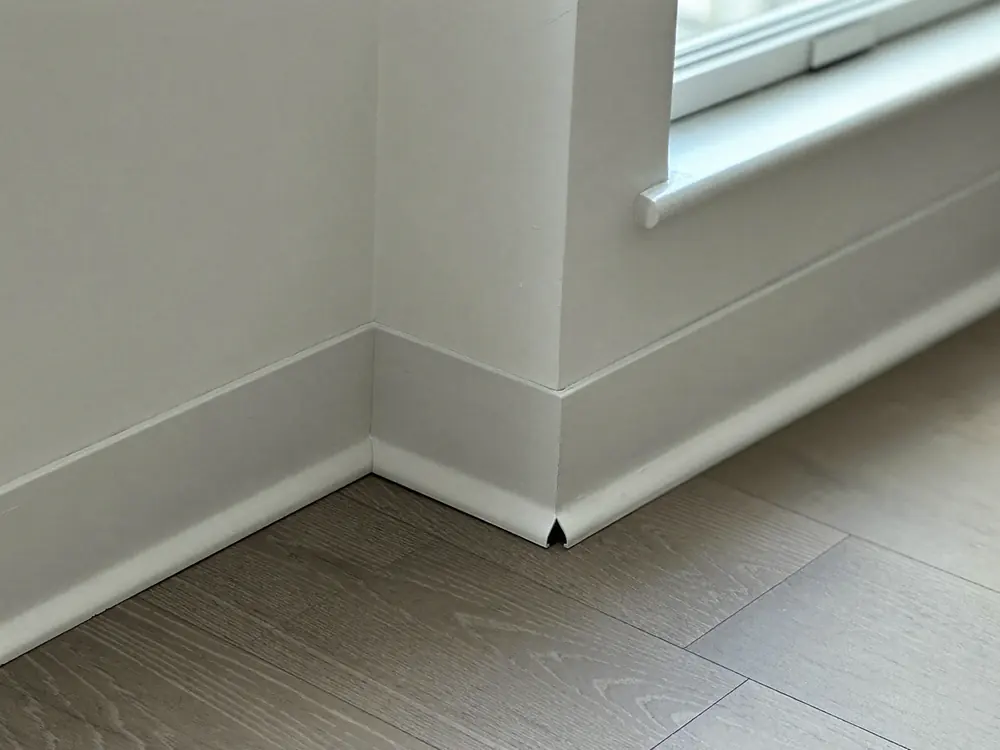 Witte plint wordt gemonteerd boven een nieuwe PVC vloer